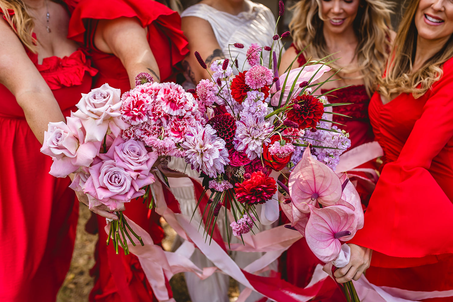Group of women in red dresses holding bouquets of flowers.